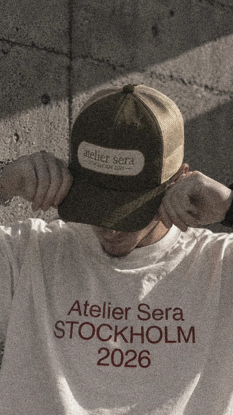 Atelier Sera Stockholm 2026 cap worn from the front, showing the embroidered badge on the moss and khaki trucker cap.
